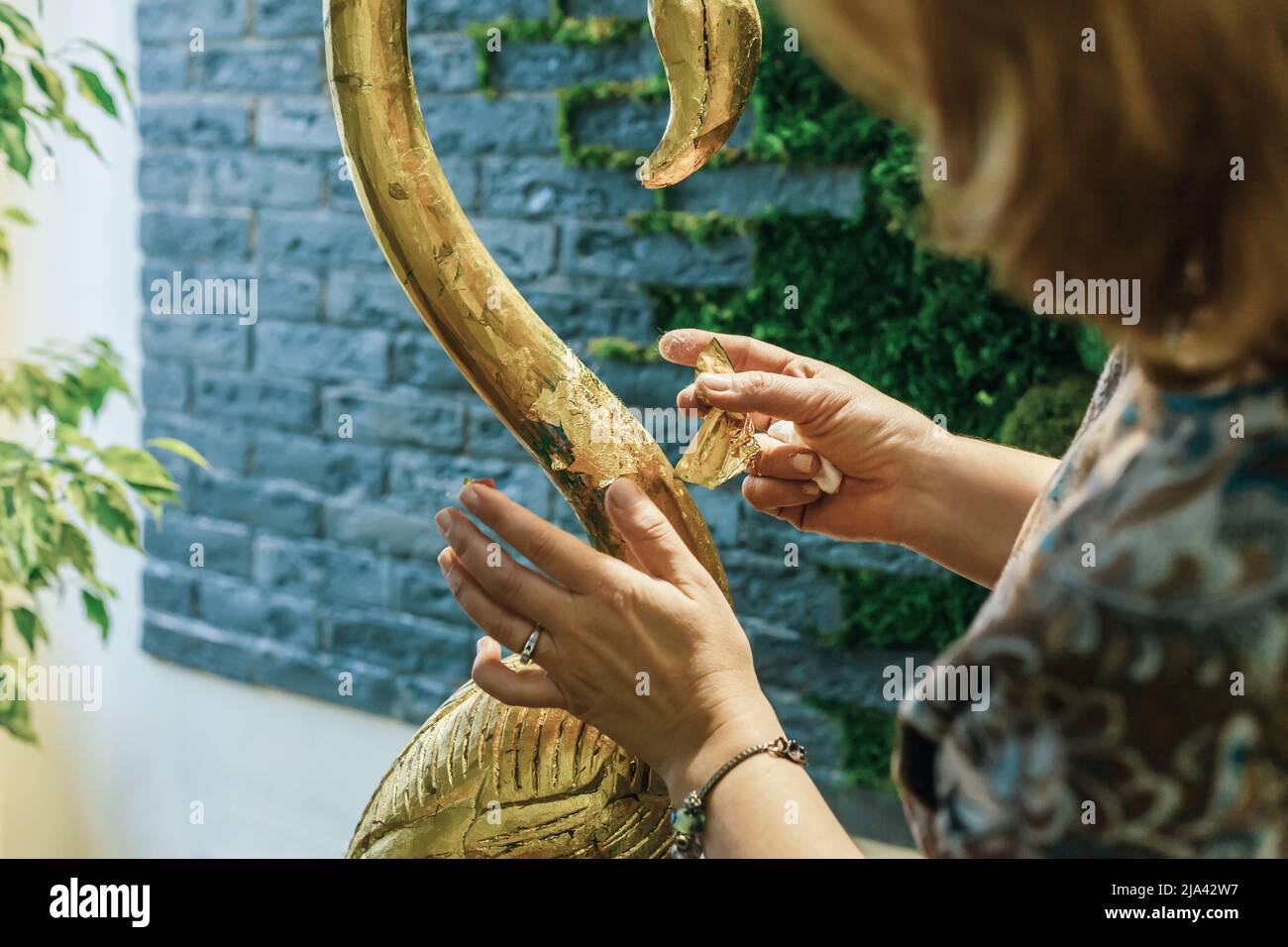 Eine Designerin restauriert und bedeckt eine hölzerne Flamingo-Statuette mit Goldfolie. Der Prozess der manuellen Vergoldung Stockfoto