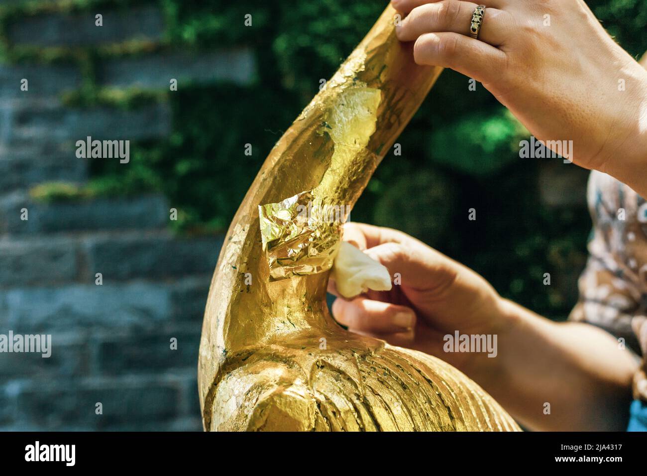 Eine Designerin restauriert und bedeckt eine hölzerne Flamingo-Statuette mit Goldfolie. Der Prozess der manuellen Vergoldung Stockfoto