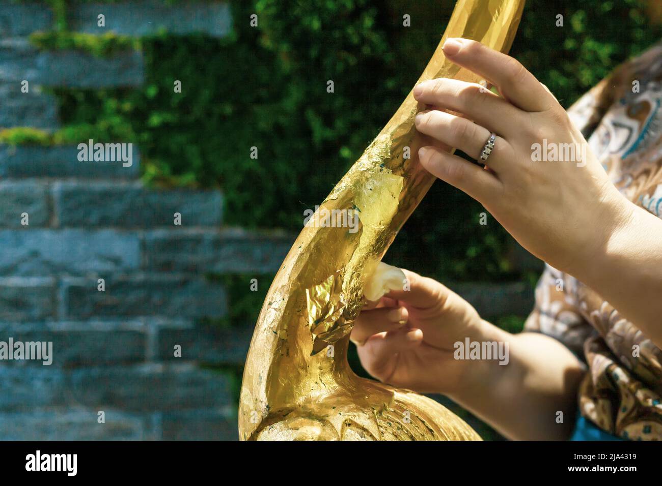 Eine Designerin restauriert und bedeckt eine hölzerne Flamingo-Statuette mit Goldfolie. Der Prozess der manuellen Vergoldung Stockfoto