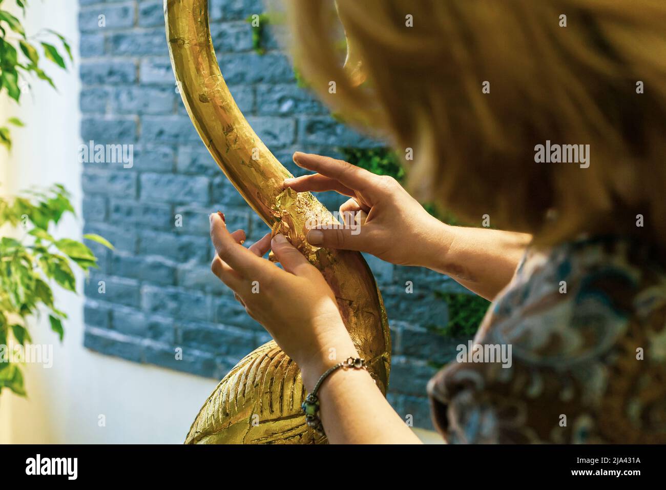 Eine Designerin restauriert und bedeckt eine hölzerne Flamingo-Statuette mit Goldfolie. Der Prozess der manuellen Vergoldung Stockfoto