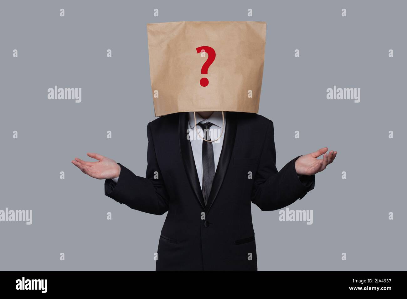 Der junge Geschäftsmann verhüllte sein Gesicht mit einer Bastelpapiertasche mit rot gezeichneter Fragestellung, wie eine Maske, um seine Identität zu verbergen. Mann isoliert auf grauem w Stockfoto