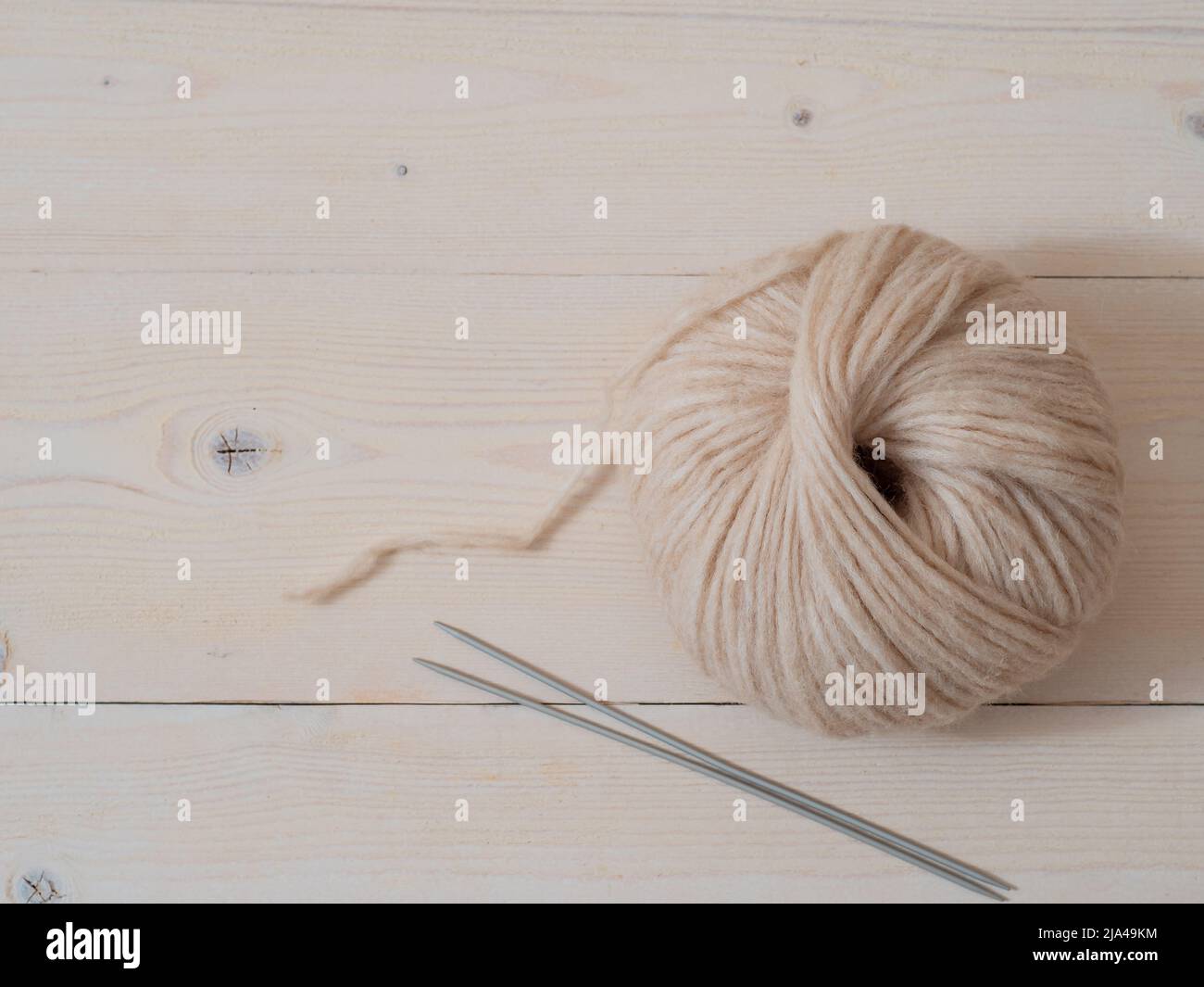 Ästhetisches Bild von beigefarbenem hellem, luftigem Garn-Skein. Mitteldickes Blasgarn aus Baby-Alpaka und Merinowolle auf Holzhintergrund. Stricknadeln kleben und Knäuel aus Garn. Speicherplatz kopieren Stockfoto