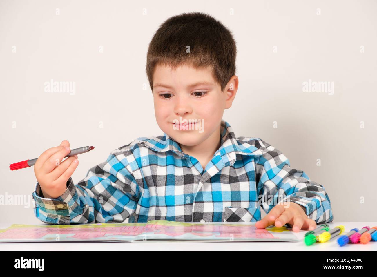 Ein Junge im Vorschulalter studiert und passiert Labyrinthe auf weißem Hintergrund. Vorbereitung für die Schule für Kinder. Stockfoto