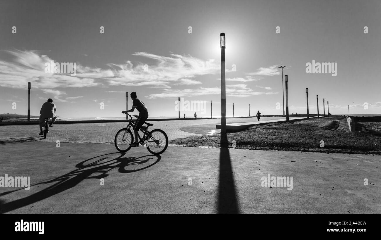 Strand Ozean Morgen öffentliche Promenade Radfahrer Läufer Silhouetten gegen Himmel eine schwarz-weiße Landschaft. Stockfoto
