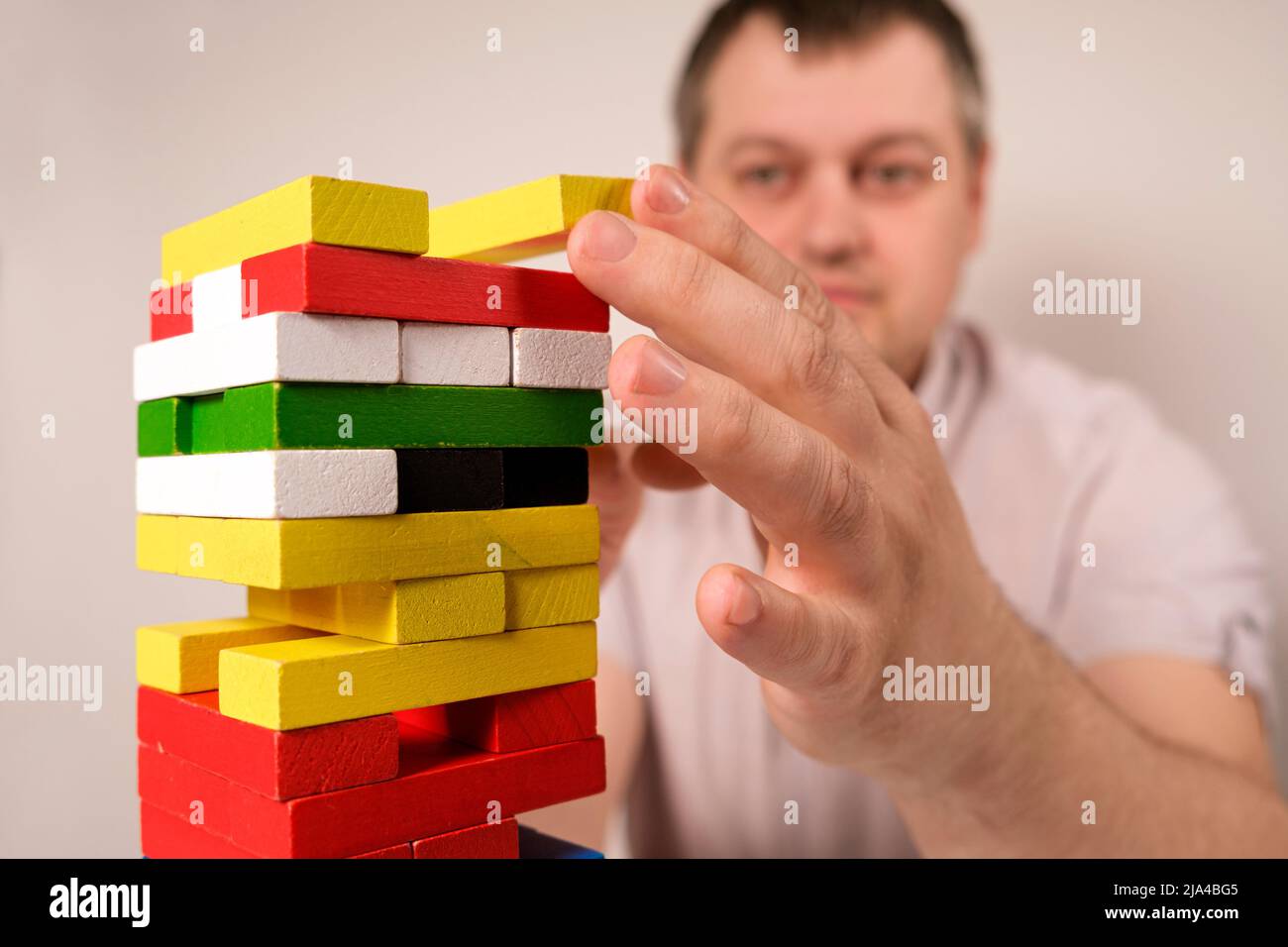 Ein Mann spielt ein Brettspiel von Jenga, zieht vorsichtig mehrfarbige Blöcke aus dem Turm. Stockfoto