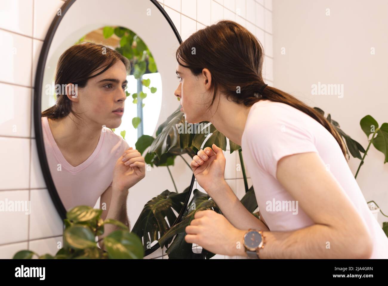 Nicht-binäre Trans-Frau, die ihre Spiegelung im Spiegel im Badezimmer zu Hause betrachtet Stockfoto
