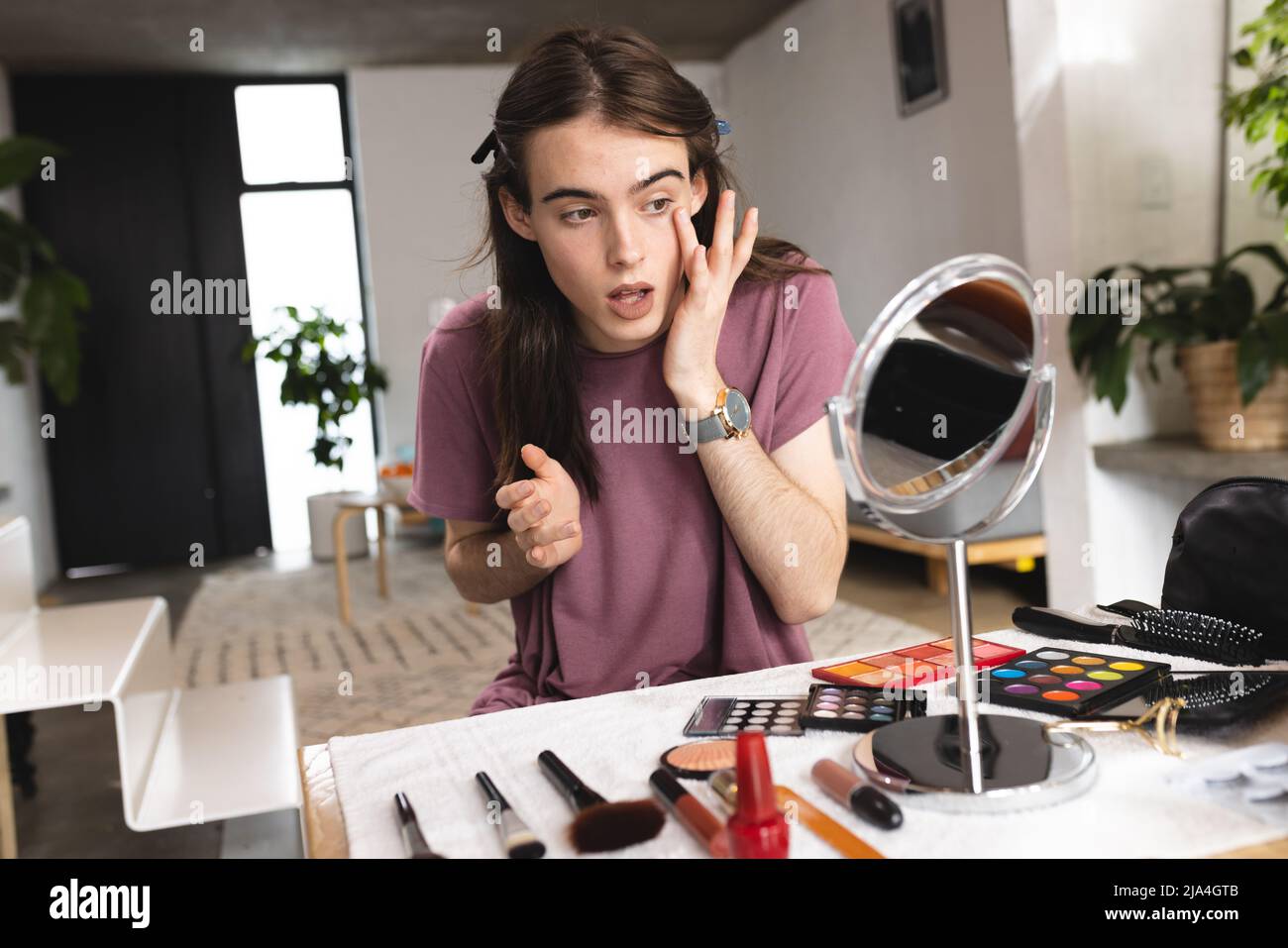 Nicht-binäre trans Frau dabei Make-up Blick in den Make-up-Spiegel zu Hause Stockfoto