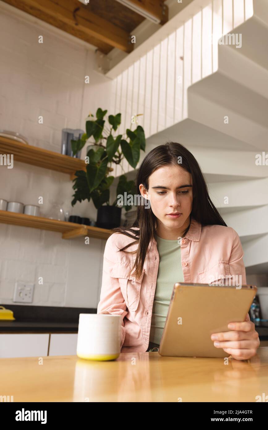 Nicht-binäre Transfrau mit Kaffeetasse mit digitalem Tablet in der Küche zu Hause Stockfoto