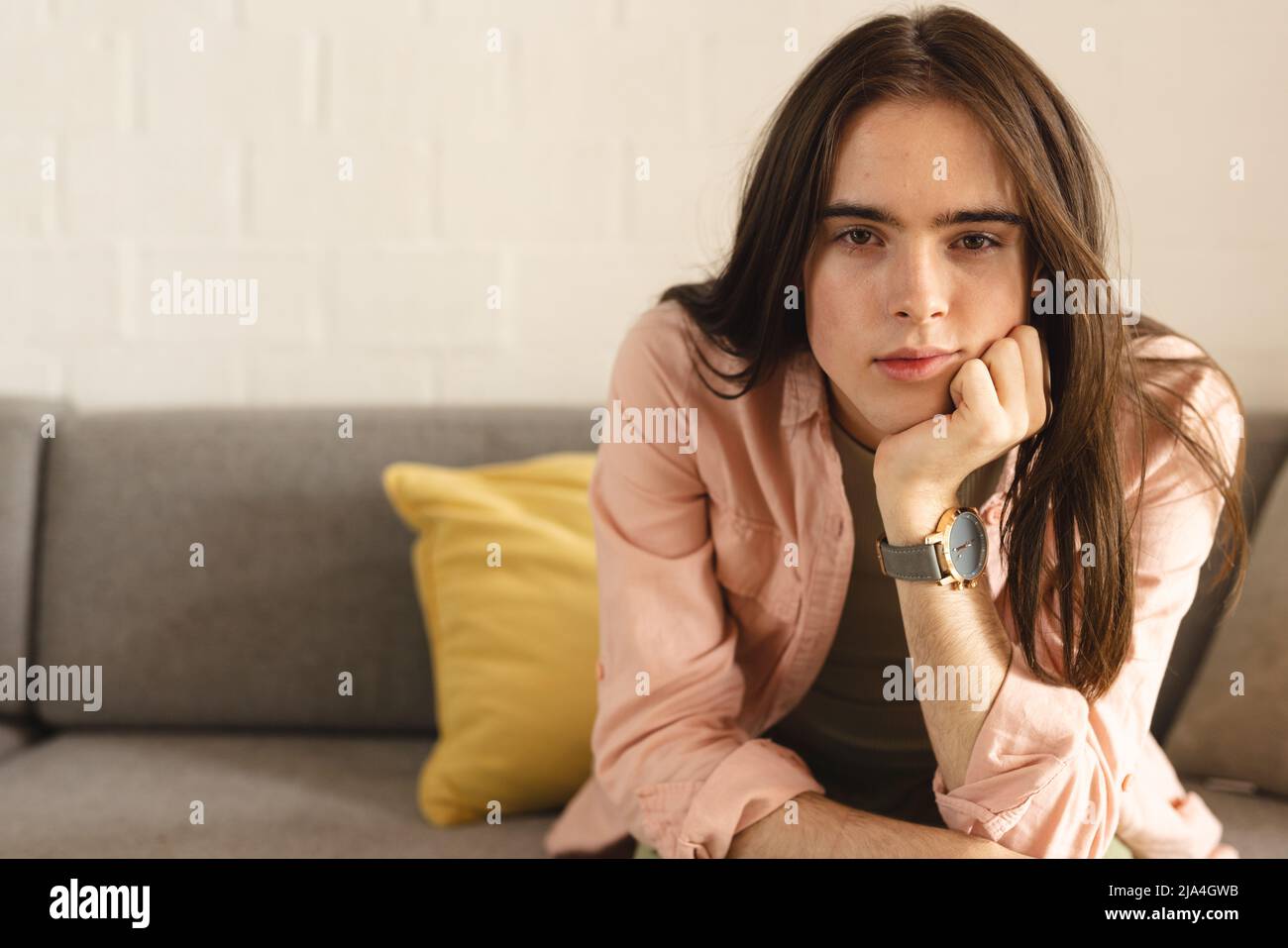 Porträt einer nachdenklichen nicht-binären Transfrau mit der Hand am Kinn, die zu Hause auf der Couch sitzt Stockfoto