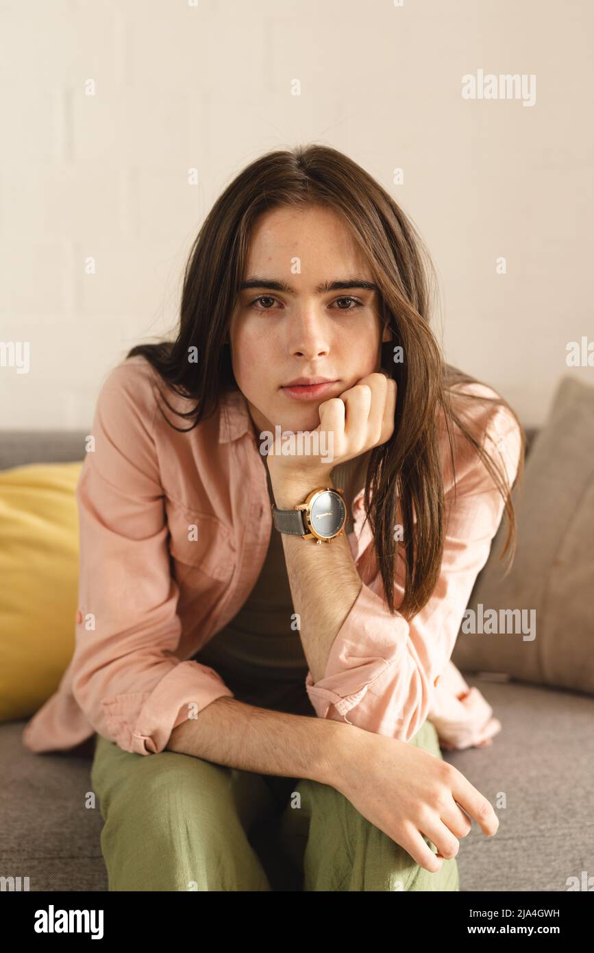 Porträt einer nachdenklichen nicht-binären Transfrau mit der Hand am Kinn, die zu Hause auf der Couch sitzt Stockfoto
