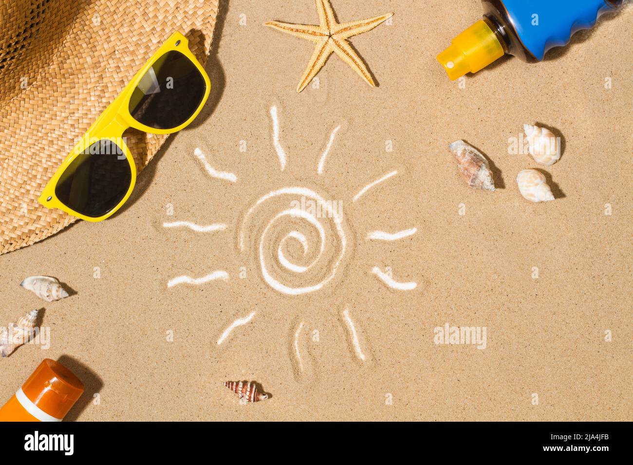 Sonnencreme-Flaschen und eine Zeichnung der Sonne auf dem Sand Stockfoto