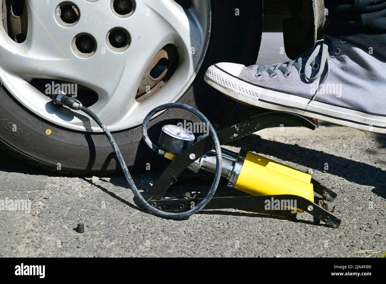 Person, die den Reifendruck im Fahrzeug überprüft und den Reifen mit dem Fuß aufbläst Pumpe Stockfoto