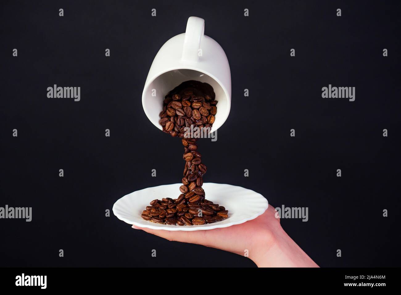 Magische Kaffeebohne spritzt aus einer Tasse mit Teller auf schwarzem Hintergrund Stockfoto