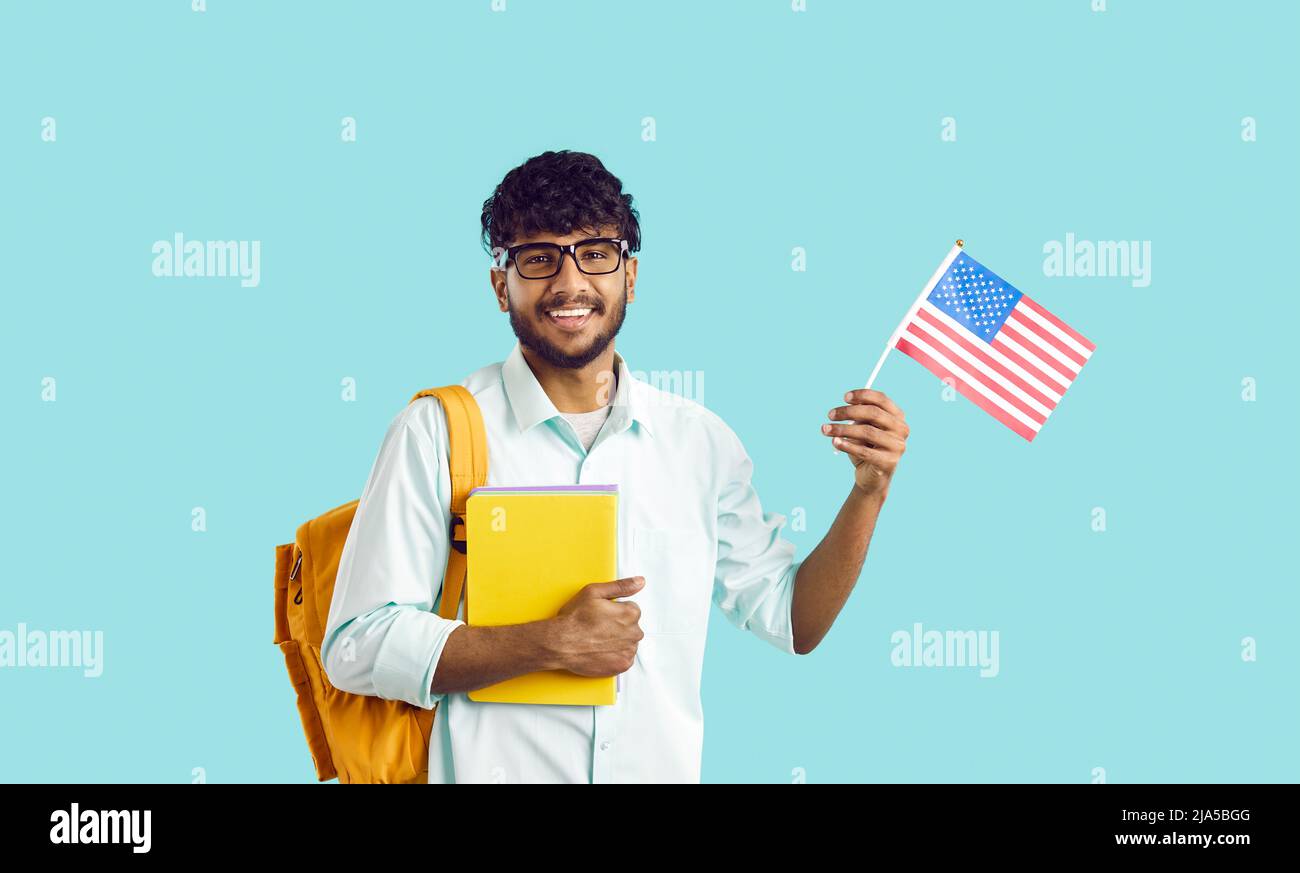 Glücklicher indischer Student, der an der amerikanischen Universität studiert und die Flagge der USA hält und lächelt Stockfoto