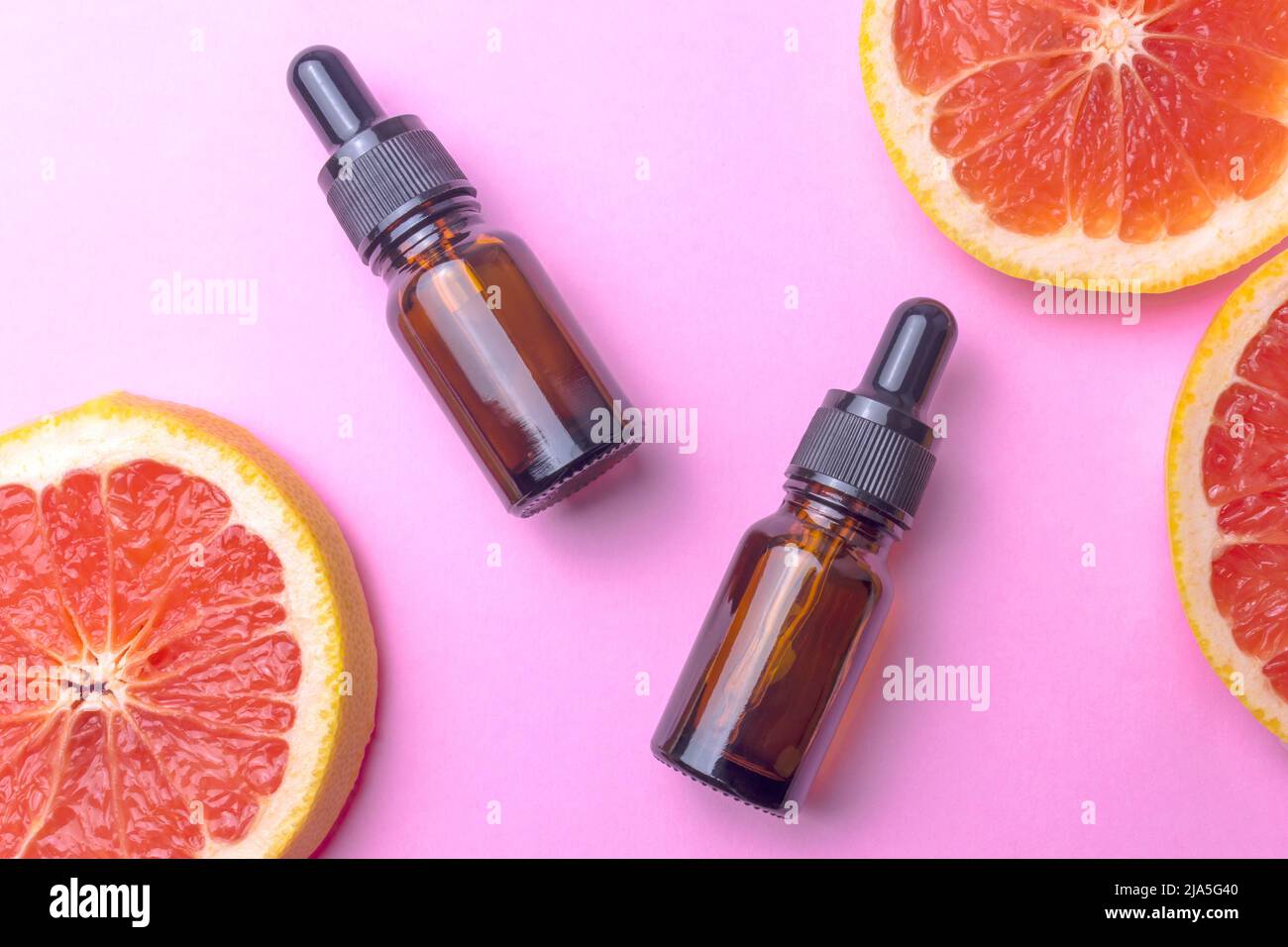 Ätherisches Grapefruitöl mit frischen Grapefruitscheiben und zwei glasbraunen Flaschen mit schwarzer Pipette Stockfoto