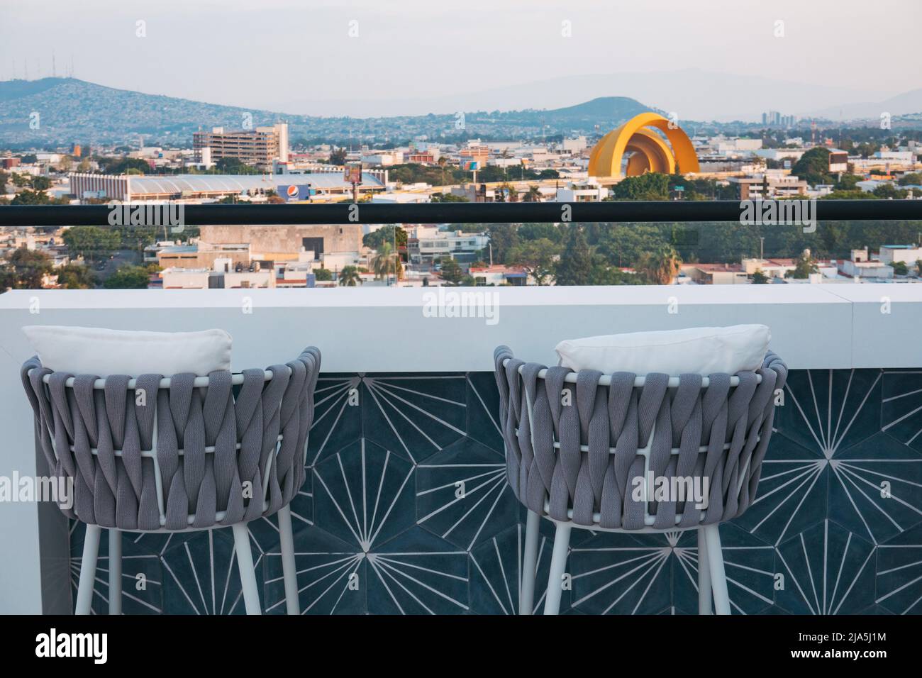 Hocker und ein Bartisch blicken vom Dach eines neuen Apartmentkomplexes in Jardines del Bosque, Guadalajara, Mexiko, auf die Skyline Stockfoto