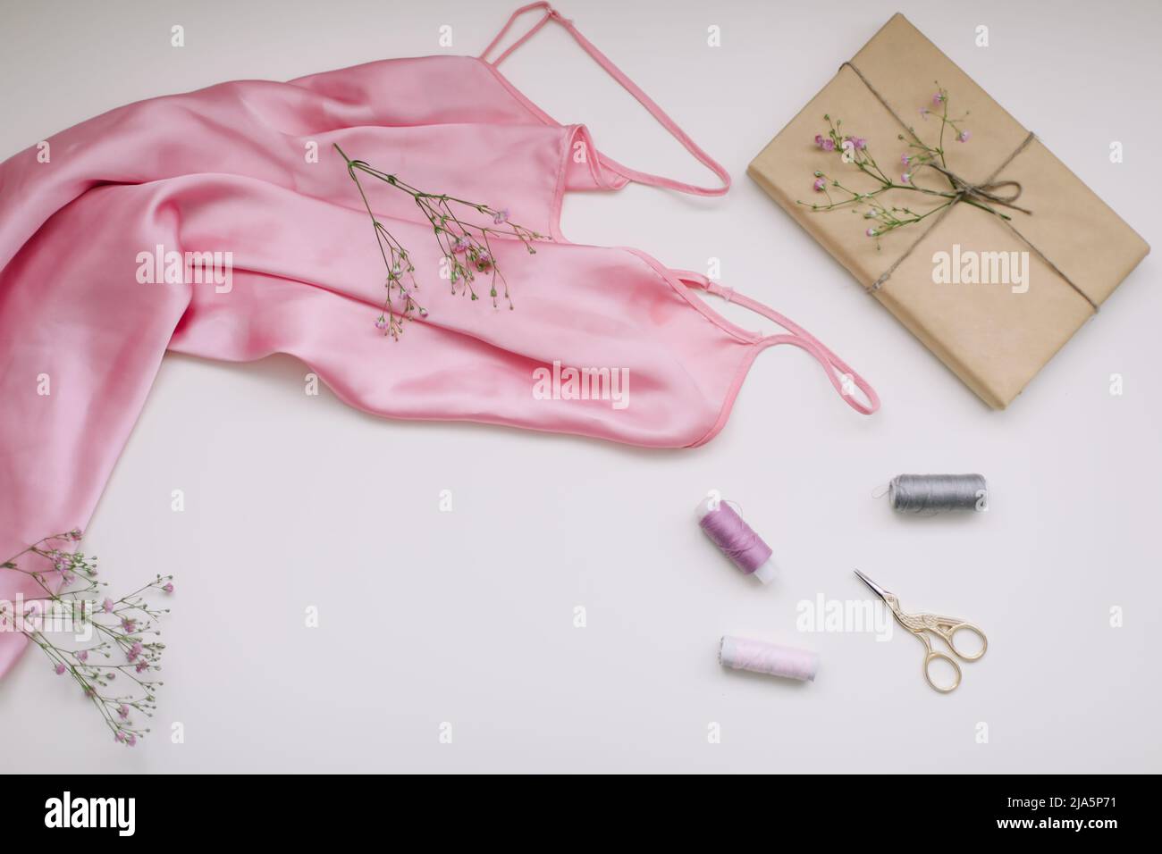 Komposition aus rosa Seidenstoff, Geschenk in Bastelpapier und Fäden und Schere auf weißem Hintergrund. Flach liegend, Draufsicht. Hobby, Freizeitkonzept. Stockfoto