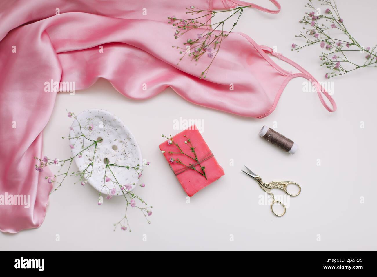 Komposition aus rosa Seidenstoff, Geschenk in Bastelpapier und Fäden und Schere auf weißem Hintergrund. Flach liegend, Draufsicht. Hobby, Freizeitkonzept. Stockfoto