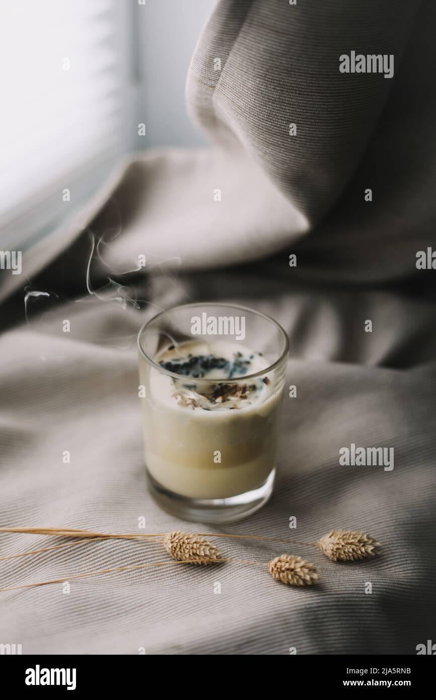 Aromatische Duftkerze mit Rauch auf beigem Textilhintergrund. Stockfoto