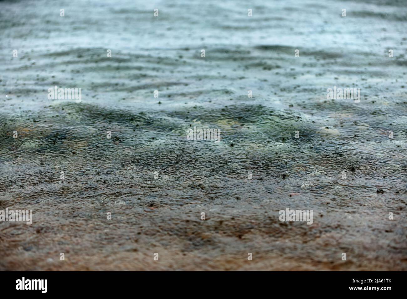 Regentropfen und Regen, die während eines starken Regenguß auf eine Seenoberfläche fallen, schaffen eine launische Atmosphäre Stockfoto