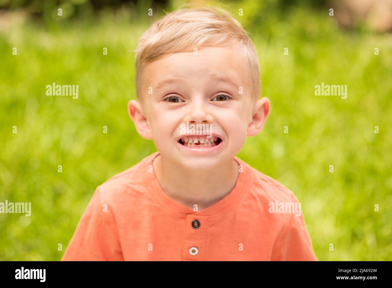 Fünfjähriger Junge, der Gesichter macht. Ein fünfjähriger blonder Junge macht Gesichter, während er bei sonnigem Wetter auf der Straße steht Stockfoto