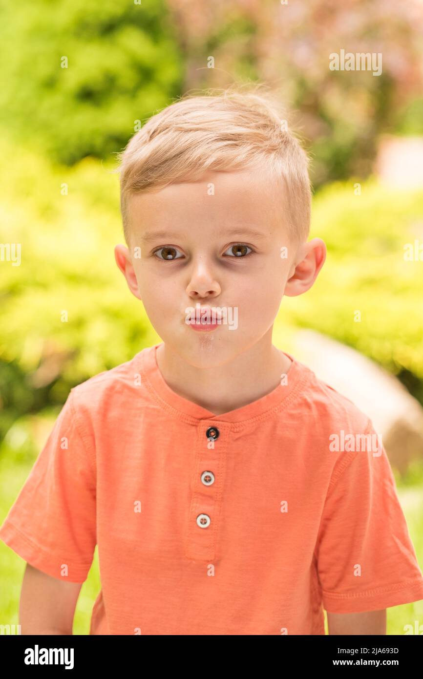 Fünfjähriger Junge, der Gesichter macht. Ein fünfjähriger blonder Junge macht Gesichter, während er bei sonnigem Wetter auf der Straße steht Stockfoto