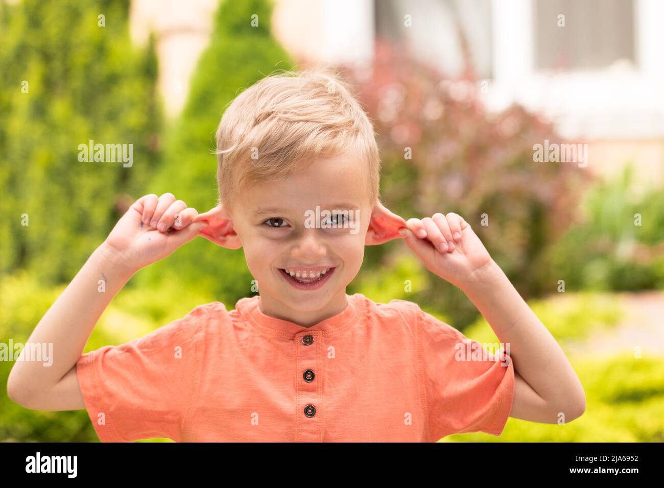 Fünfjähriger Junge, der Gesichter macht. Ein fünfjähriger blonder Junge macht Gesichter, während er bei sonnigem Wetter auf der Straße steht Stockfoto