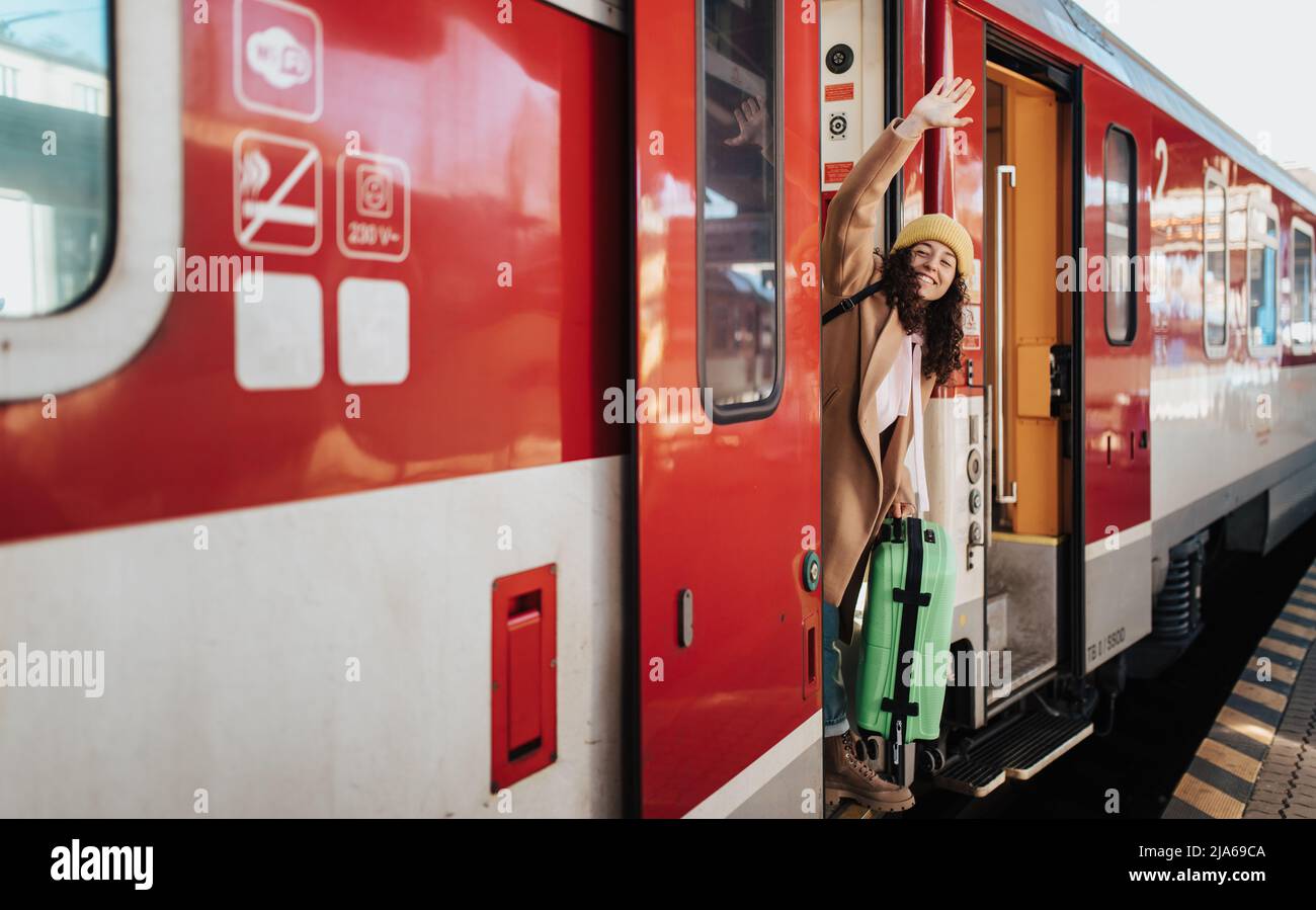 Glückliche junge Reisende Frau mit Gepäck, die am Bahnhofsplatz in den Zug steigen Stockfoto
