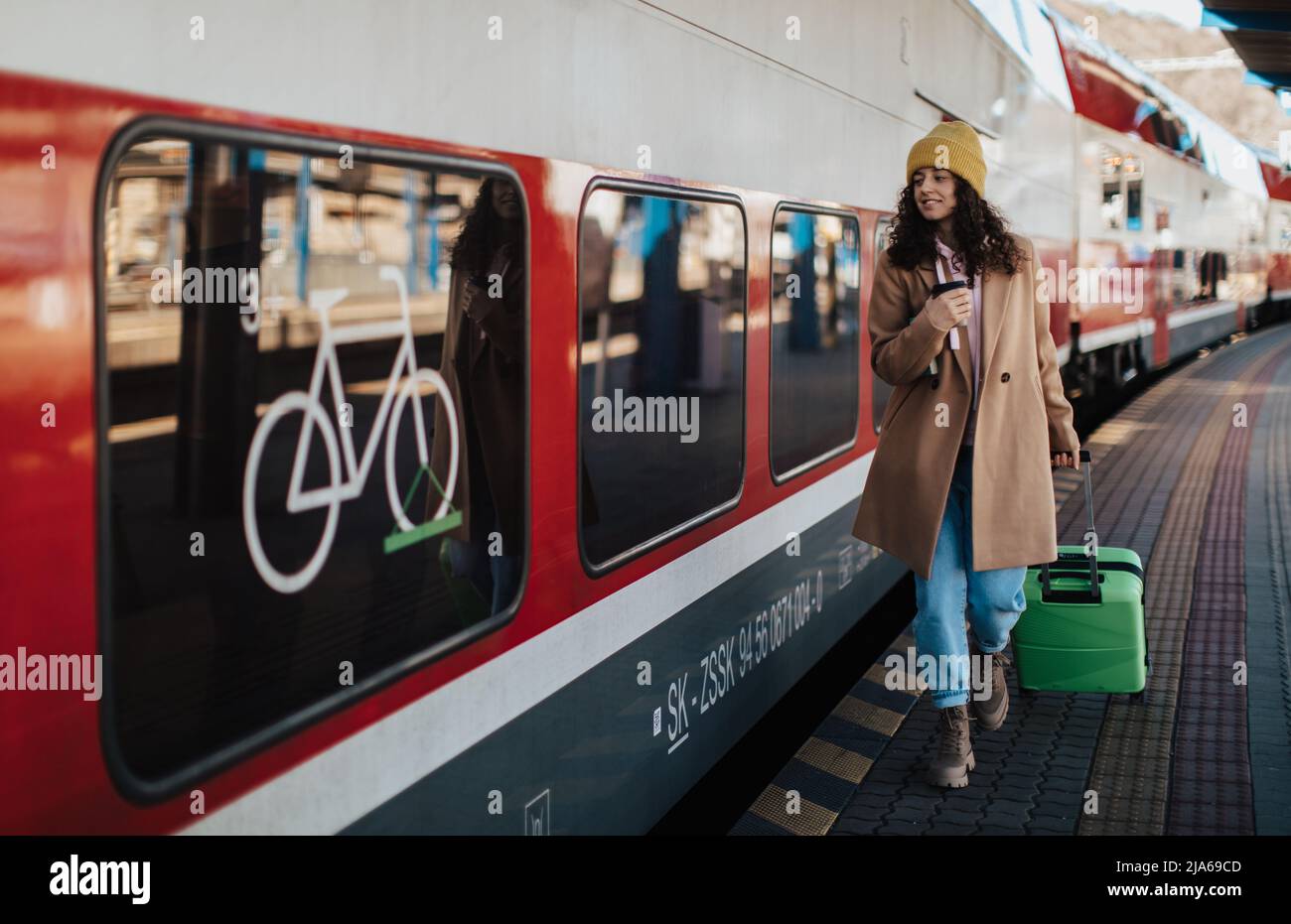Glückliche junge Reisende Frau mit Gepäck, das im Zug am Bahnsteig des Bahnhofs an Bord geht Stockfoto