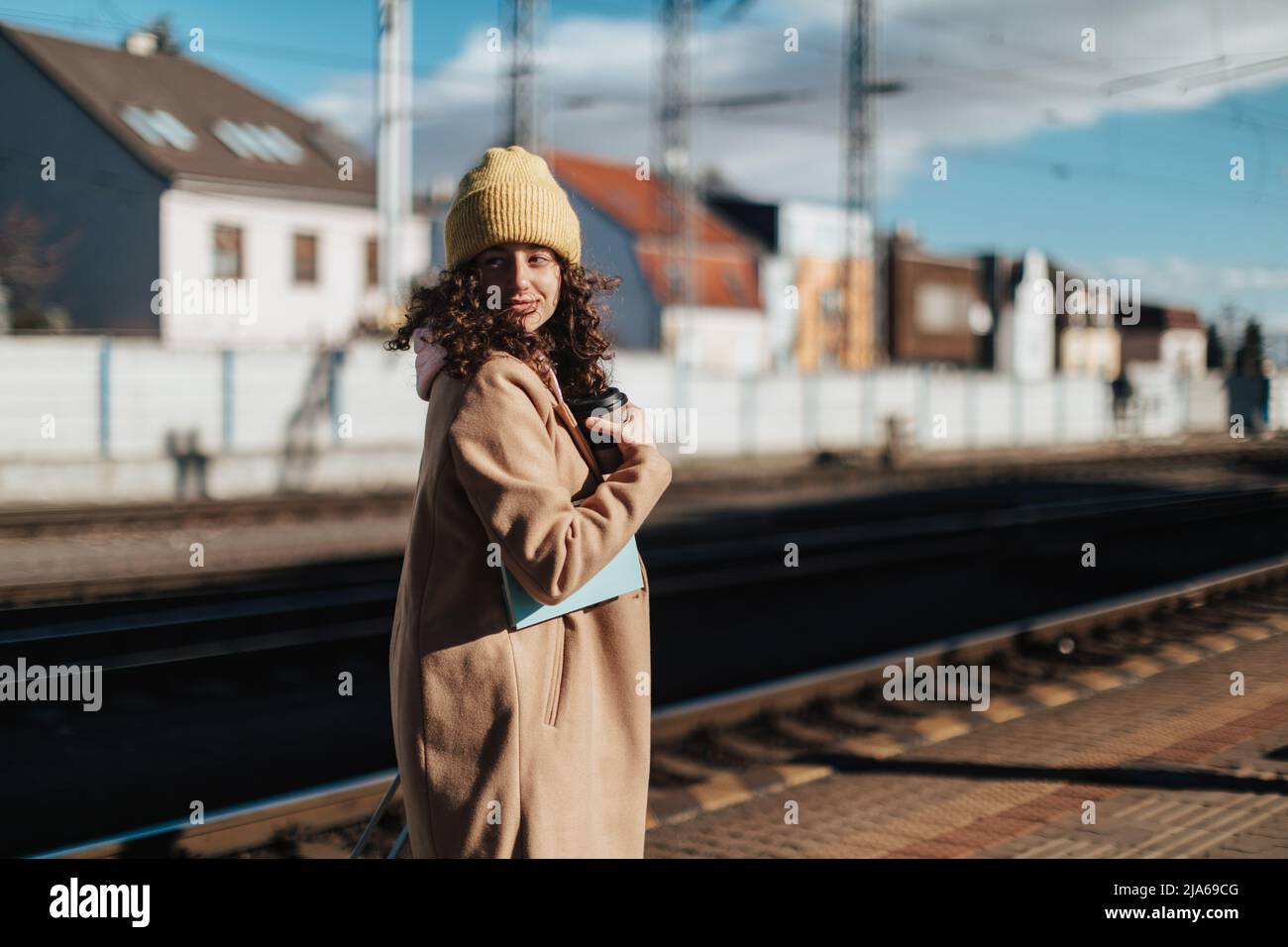 Glückliche junge Reisende Frau mit einer Tasse Kaffee am Bahnhofsplatz Stockfoto