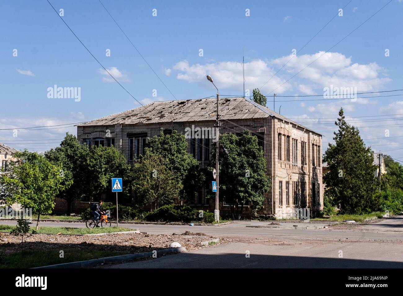 Bakhmut, Ukraine. 24.. Mai 2022. Ein Mann fährt mit dem Fahrrad an einem Wohnhaus mit einem Dach vorbei, das durch Schüsse in Bakhmut, Donbas, beschädigt wurde. Da Bakhmut als Schlüsselstadt der ukrainischen Streitkräfte bei der Verteidigung der Donezker Region steht, wird die Stadt von russischen Truppen angegriffen. Die russische Invasion der Ukraine begann am 24. Februar, dem Krieg, der zahlreiche Zivilisten und Soldaten getötet hat. Kredit: SOPA Images Limited/Alamy Live Nachrichten Stockfoto