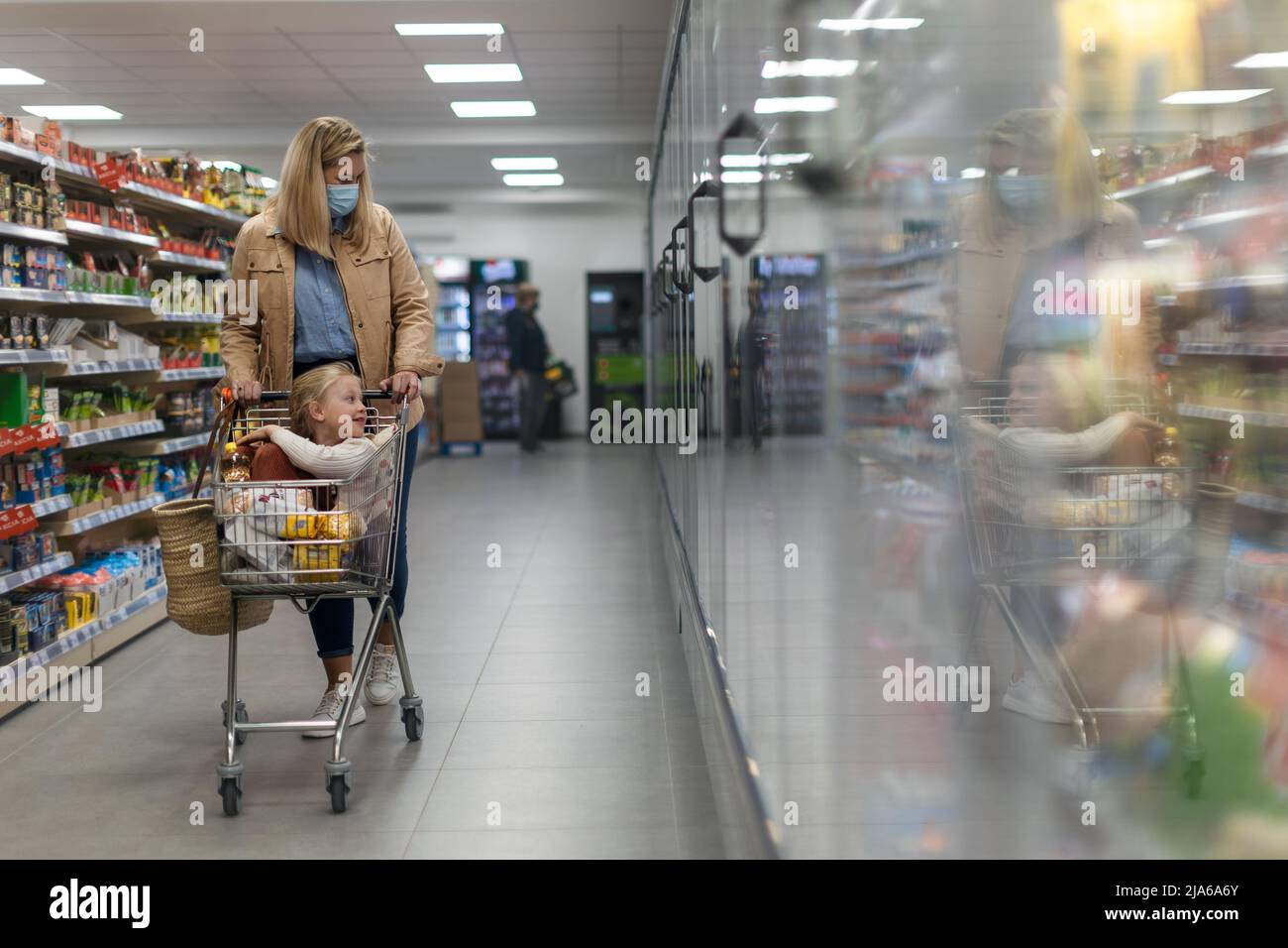 Kleines Mädchen, das beim Einkaufen mit ihrer Mutter im Supermarkt auf dem Trolley sitzt Stockfoto