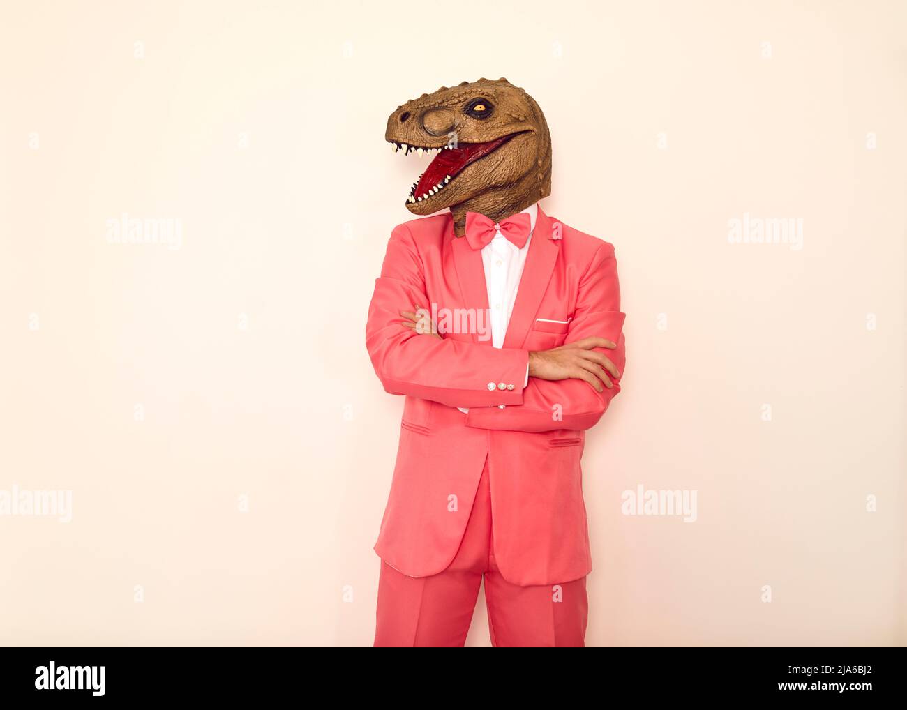 Seltsamer Typ in einem rosa Anzug und einer lustigen Dinosaurier-Maske, die vor einem weißen Hintergrund steht Stockfoto