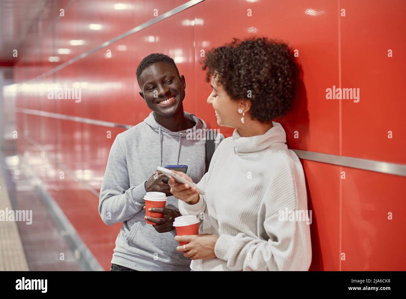 Junge Menschen mit Smartphones und Kaffee zum Mitnehmen warten auf die U-Bahn. Stockfoto