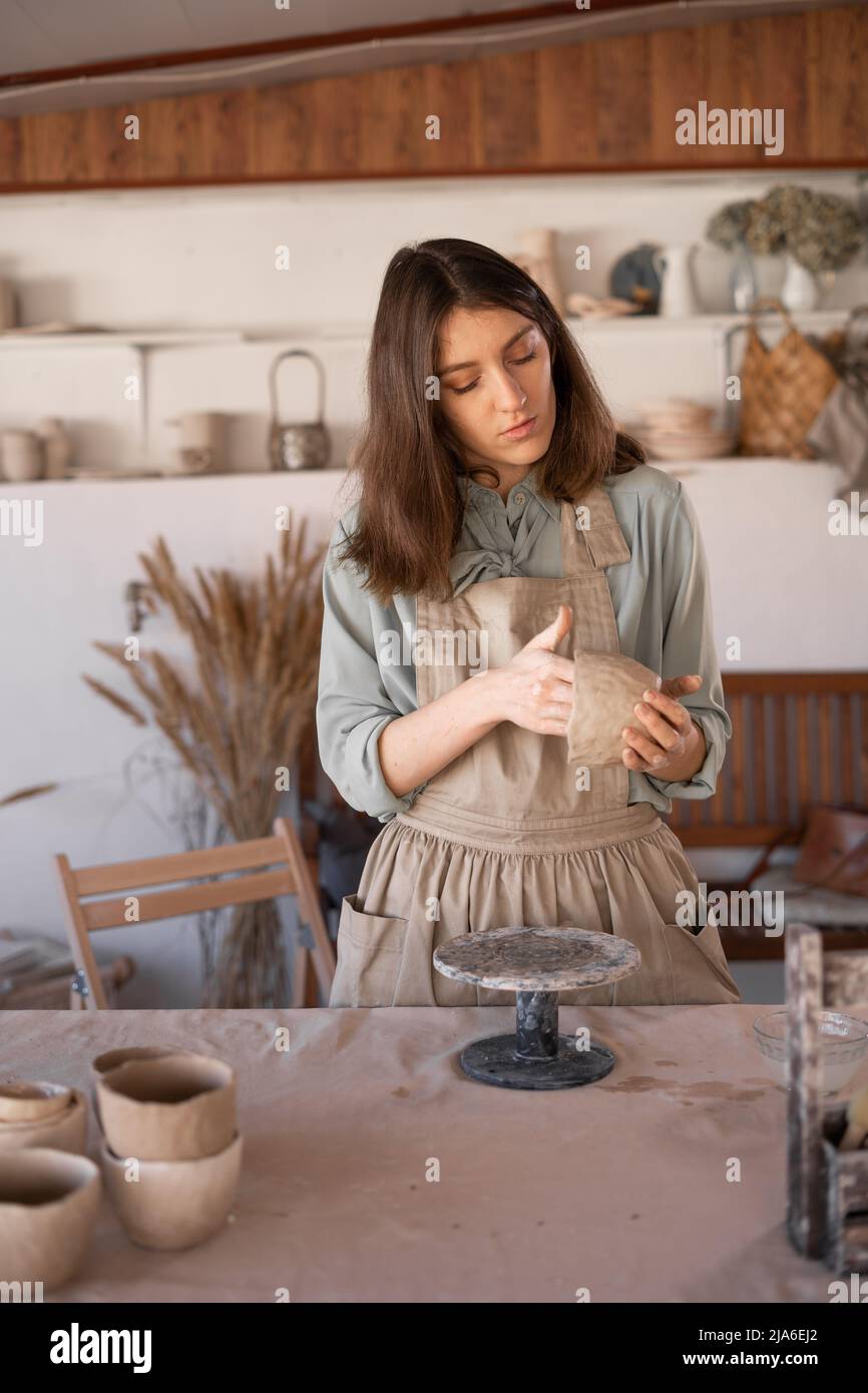Die junge Kunsthandwerkerin konzentrierte sich während eines Töpferunterrichtete oder Workshops in einem kreativen Studio auf die Bildhauerei einer rohen Tonschale. Frau Keramik Geschäftseigentümer machen Stockfoto