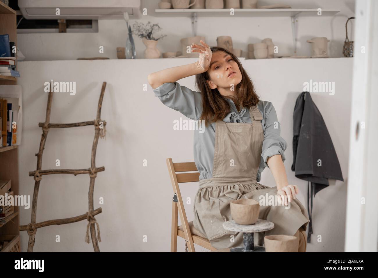 Müde kaukasische schöne weibliche Töpfer am Arbeitsplatz. Erstellung von handgefertigten Töpferwaren. Ein Töpfer in einem Keramikstudio bildet einen Topf aus nassem Ton. Damen Stockfoto