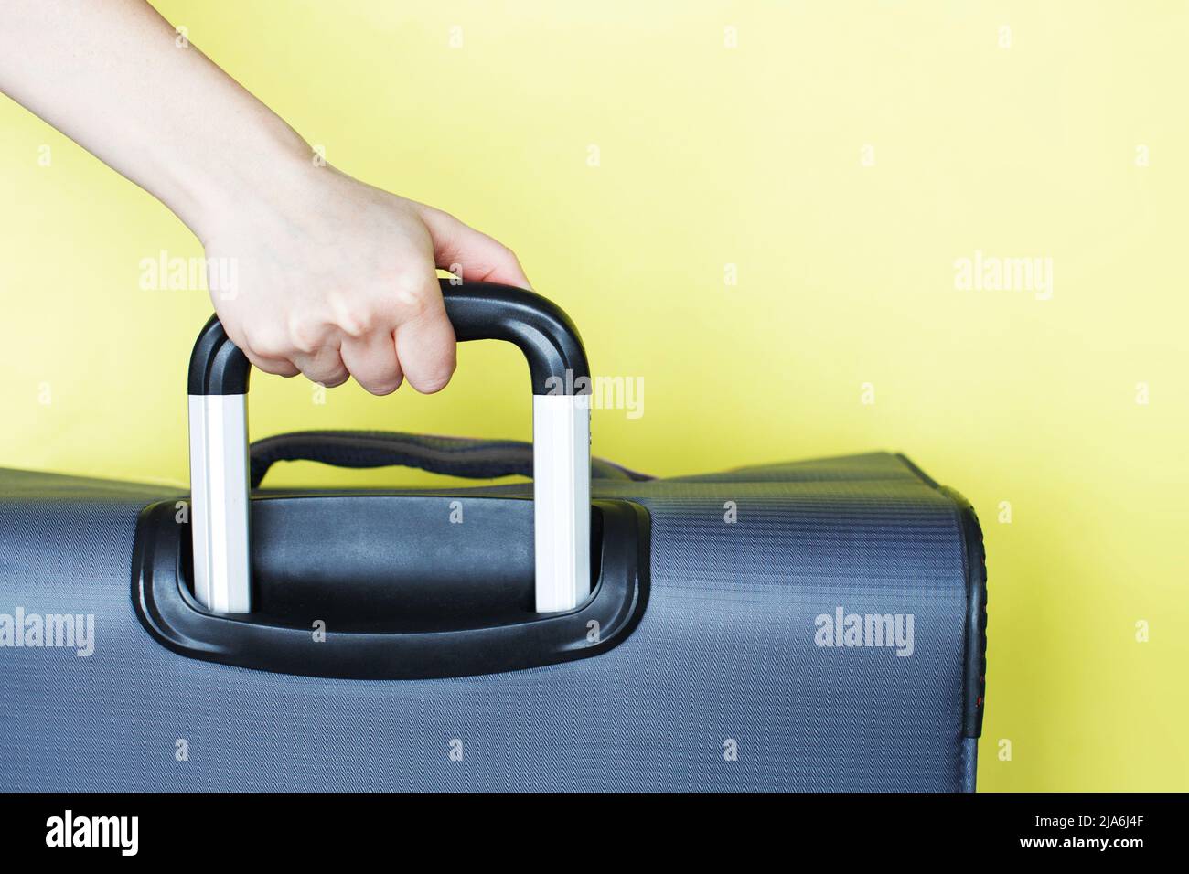 Hand hält einen Koffer isoliert auf einem gelben Hintergrund. Passagiere, die am Wochenende ins Ausland reisen. Konzept der Flugreise. Kopiere den Speicherplatz Stockfoto