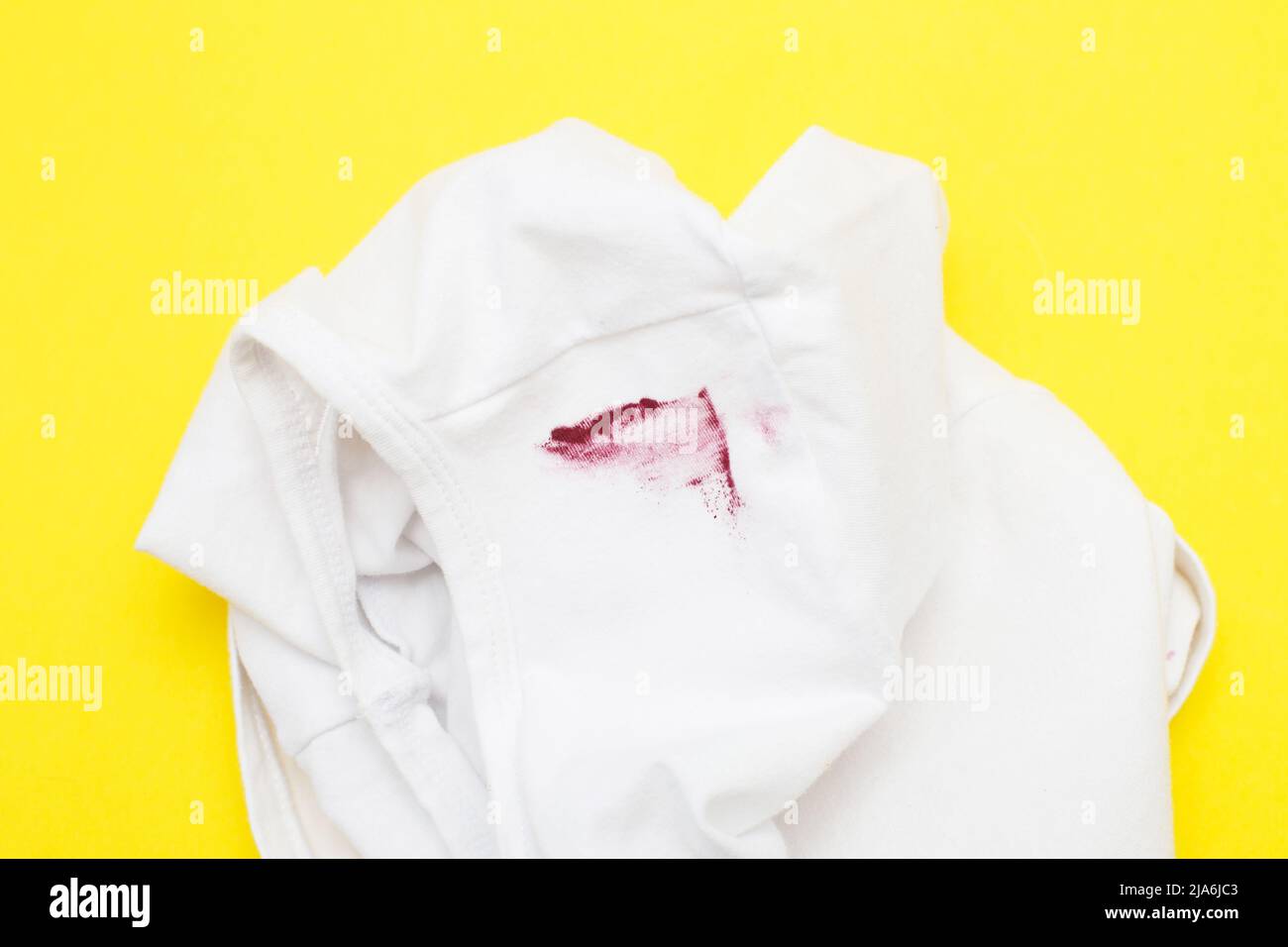 Roter Lippenstift-Fleck auf weißem Hemd auf gelbem Hintergrund. Stockfoto