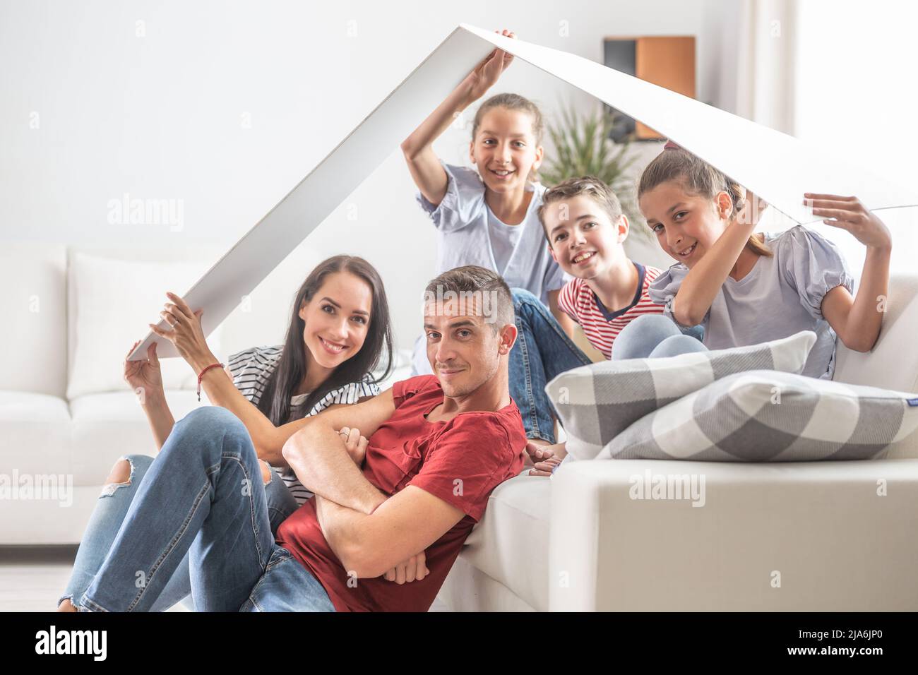 Familie mit drei Kindern sind alle glücklich unter einem symbolischen Dach zu Hause sitzen auf und um das Sofa. Stockfoto