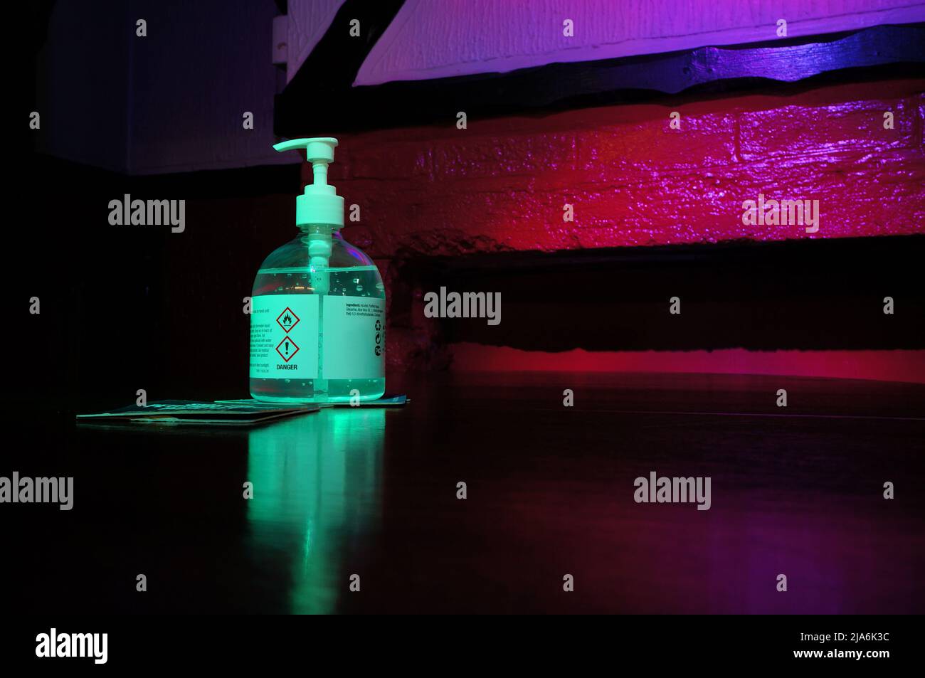 Handdesinfektionsflasche auf einem Tisch in einem Pub mit roter/grüner Beleuchtung und Platz für Text Stockfoto