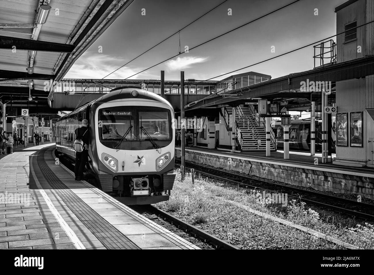 Eisenbahnzug an einem Bahnsteig. Ein Besatzungsmitglied steht an einer Tür und Schatten fallen auf die Plattform. Stockfoto