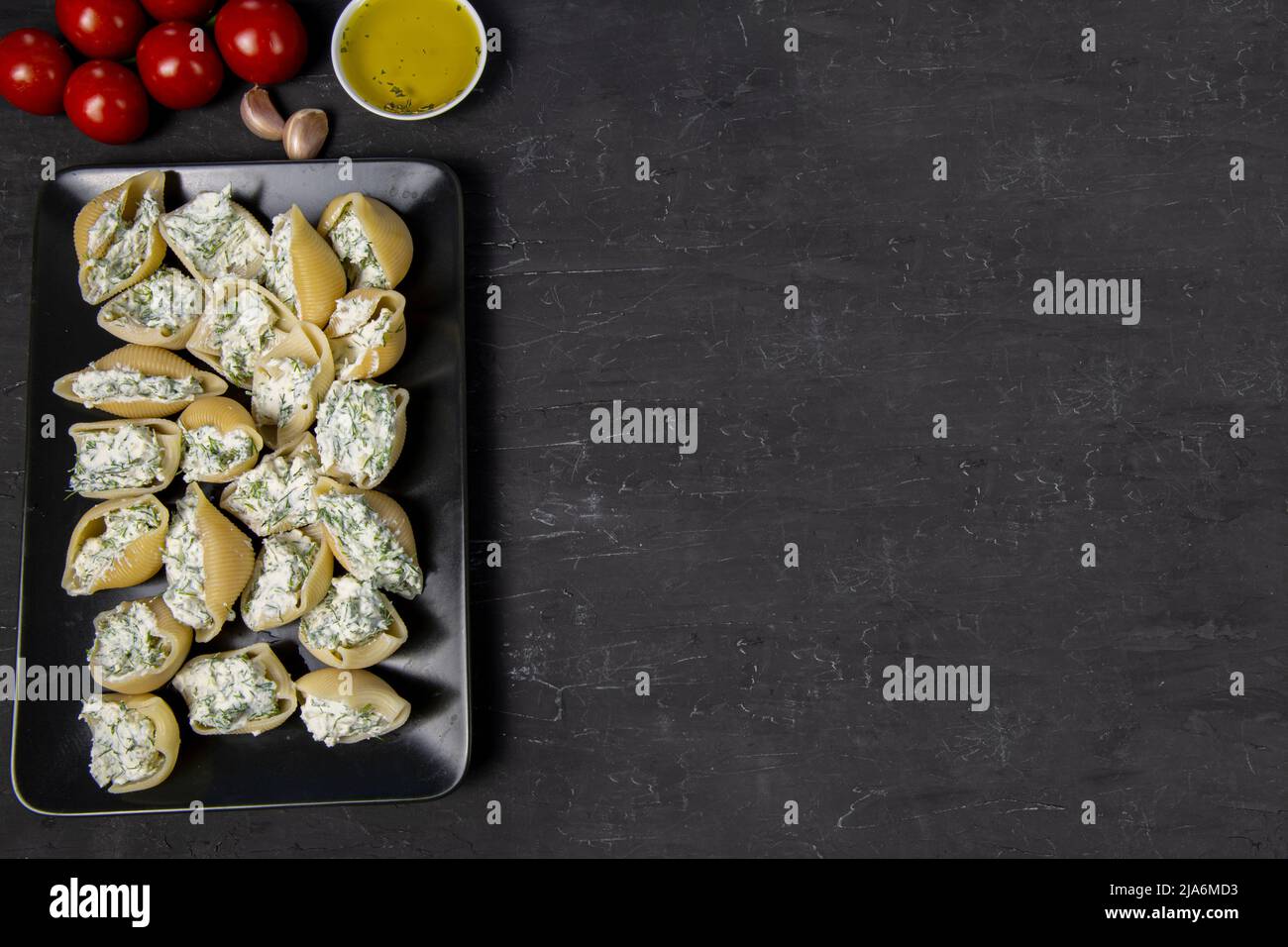 Gefüllte Conchiglie-Zubereitung, leckere italienische Küche. Platz zum Kopieren, freier Platz für Text auf schwarzem Beton-Hintergrund, Draufsicht. Stockfoto