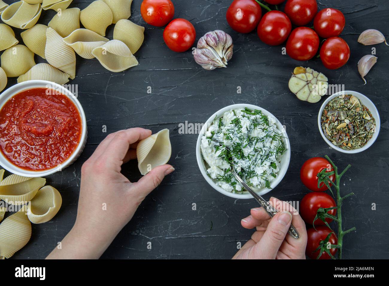 Gefüllte Conchiglie Zubereitung, Lebensmittelzutaten und weibliche Hände auf schwarzem Beton Hintergrund. Leckere itaische Küche. Stockfoto