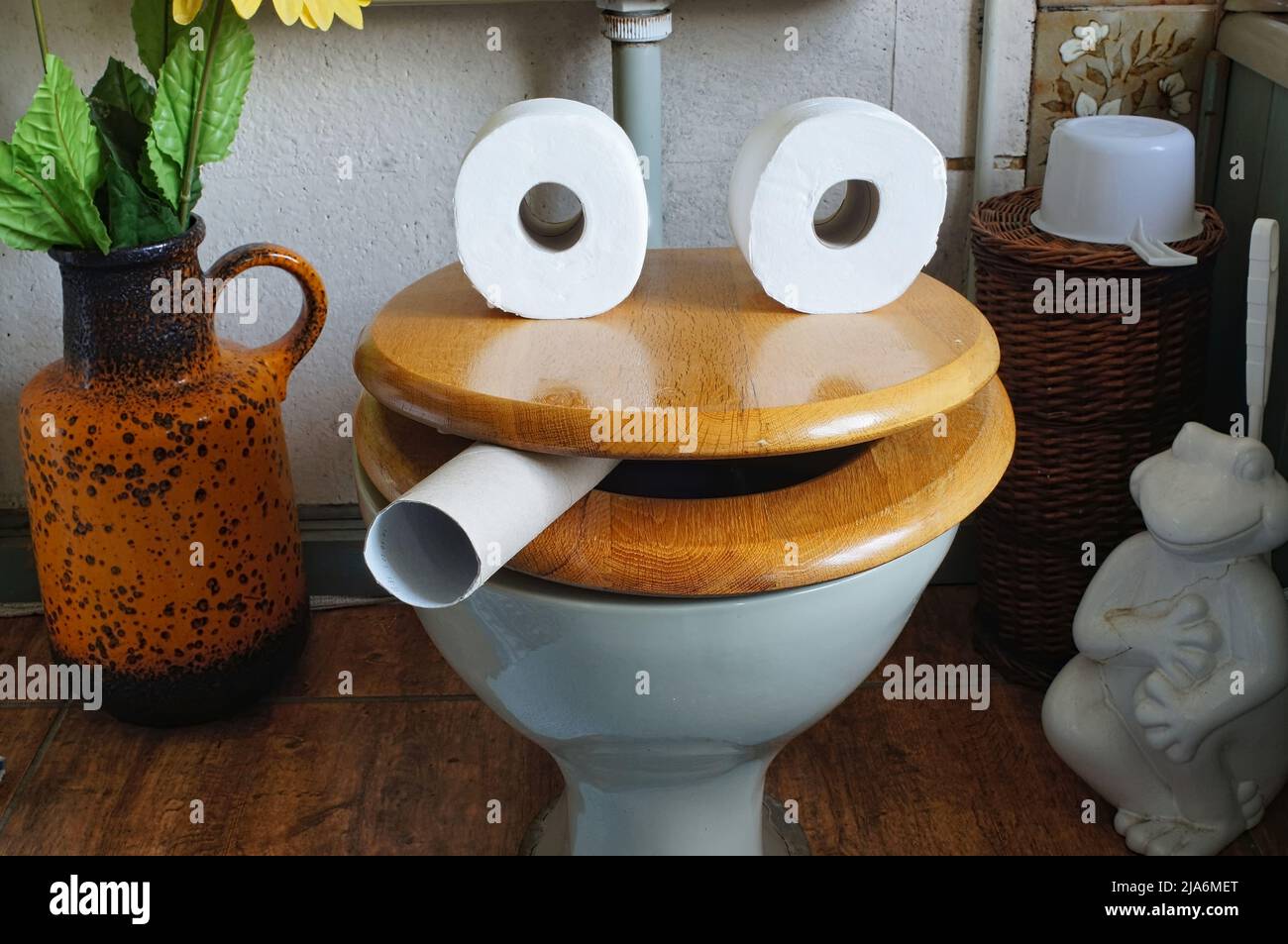 Ein lustiges Gesicht, das aus einem hölzernen Toilettensitz und einem Toilettenpapierrollen im Badezimmer entstand Stockfoto
