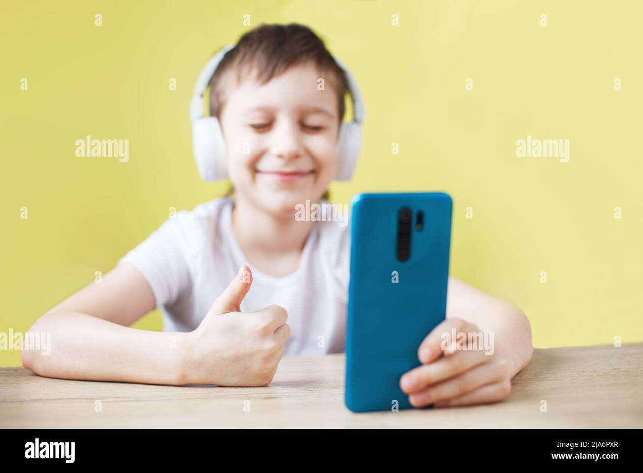 Freizeit, Kinder, Technik und Menschen Konzept - lächelnder Junge mit Smartphone und Kopfhörer mit Videoanruf zu Hause. Kind mit Handy auf einem gelben Stockfoto