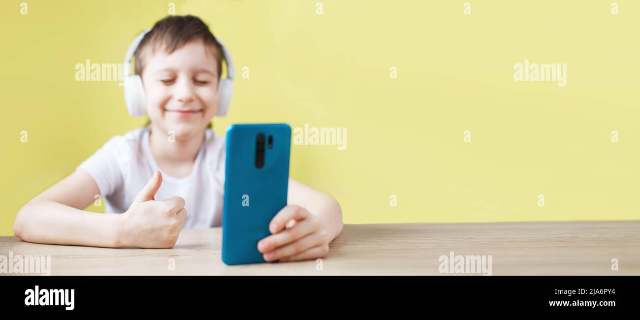 Freizeit, Kinder, Technik und Menschen Konzept - lächelnder Junge mit Smartphone und Kopfhörer mit Videoanruf zu Hause. Kind mit Handy auf einem gelben Stockfoto