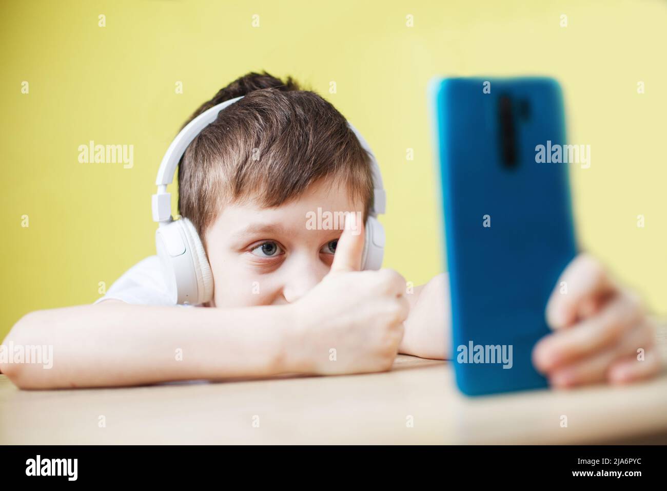 Freizeit, Kinder, Technik und Menschen Konzept - lächelnder Junge mit Smartphone und Kopfhörer mit Videoanruf zu Hause. Kind mit Handy auf einem gelben Stockfoto
