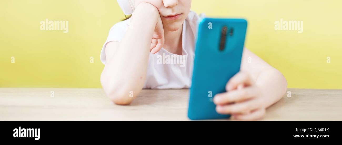 Freizeit, Kinder, Technik und Menschen Konzept - lächelnder Junge mit Smartphone und Kopfhörer mit Videoanruf zu Hause. Kind mit Handy auf einem gelben Stockfoto