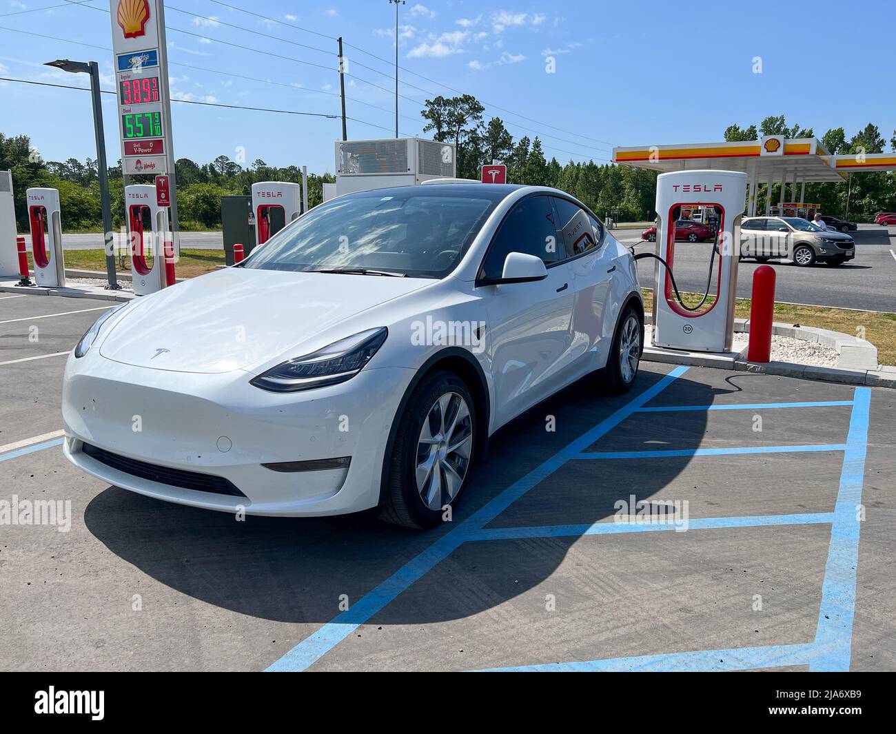 Jasper, FL USA-30. April 2022: Ein Tesla-Auto lädt an einer Tesla Supercharger Station in Florida neben einer Tankstelle mit hohen Gaspreisen. Stockfoto