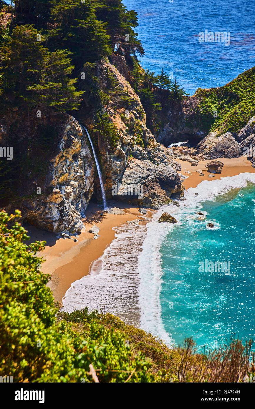 Versteckter Wasserfall an einer Sandbucht mit farbenfrohen Meereswellen Stockfoto